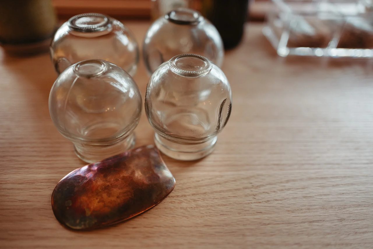 Four glass cupping cups and a polished gua sha stone on a wooden counter.