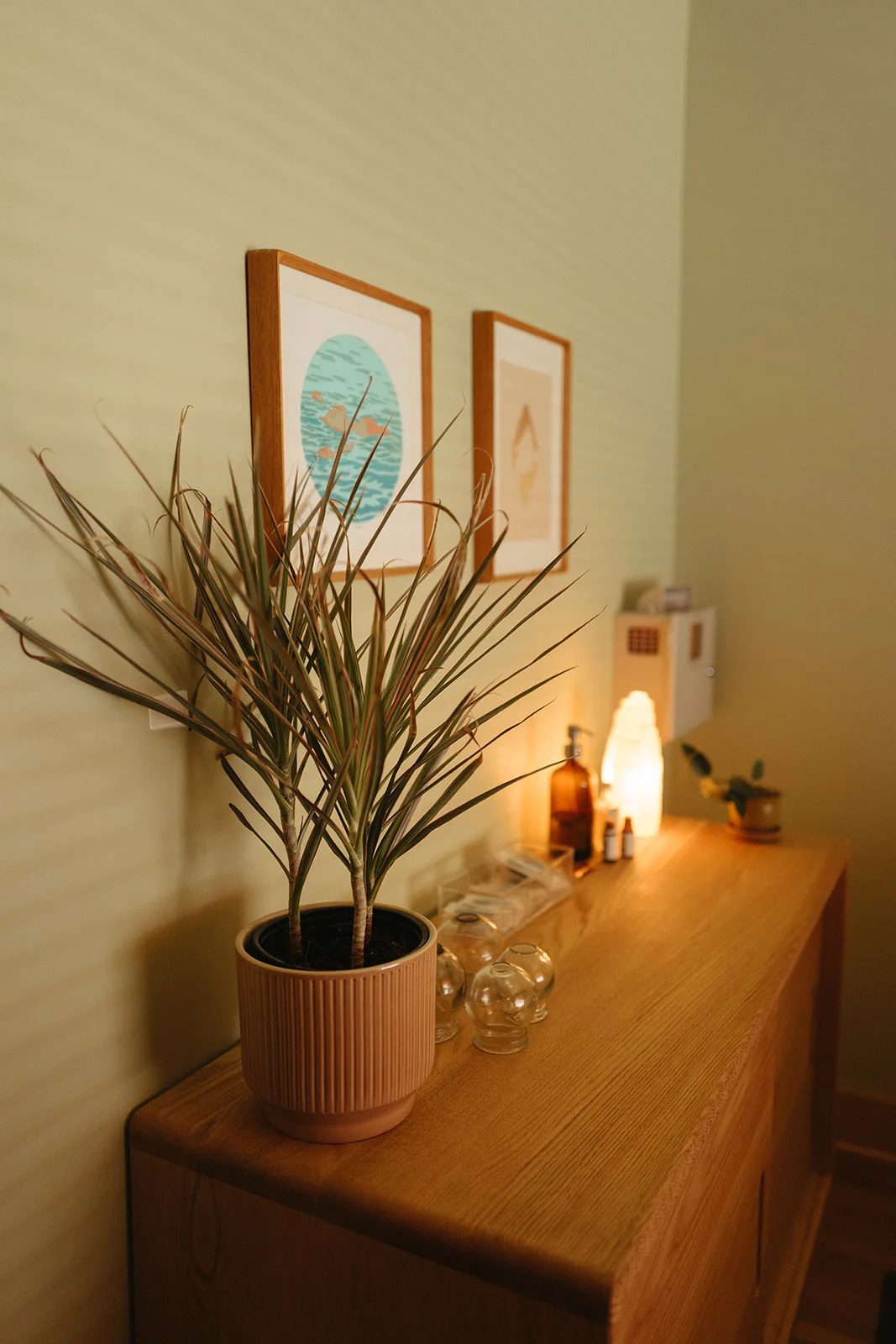 A wooden dresser in a Mandala treatment room with a trailing plant and a glowing salt lamp.