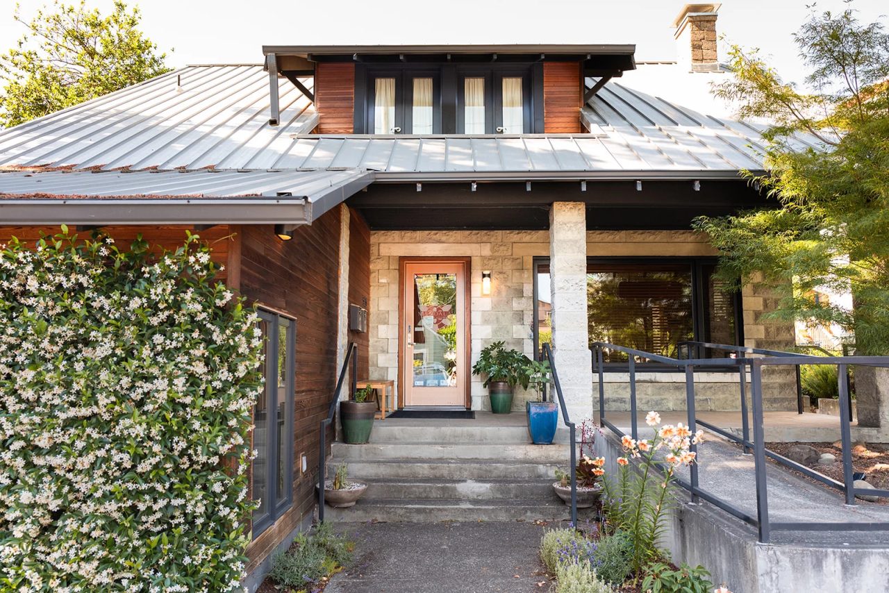 The clinic's entrance on East Burnside: steps and a ramp up to a stone porch, the front door between potted plants, star jasmine on the left.