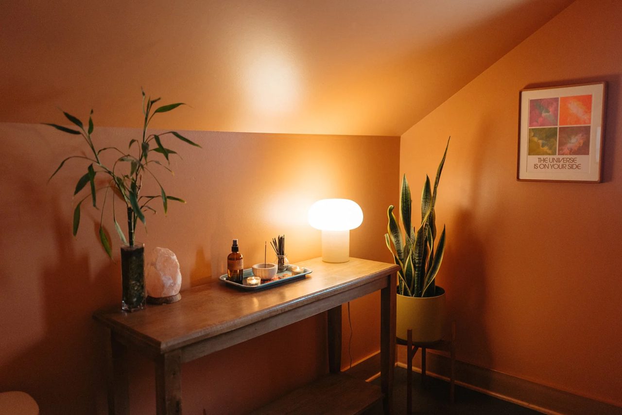 A corner table with a glowing lamp, lucky bamboo, a salt lamp and a snake plant, under a print that reads The universe is on your side.