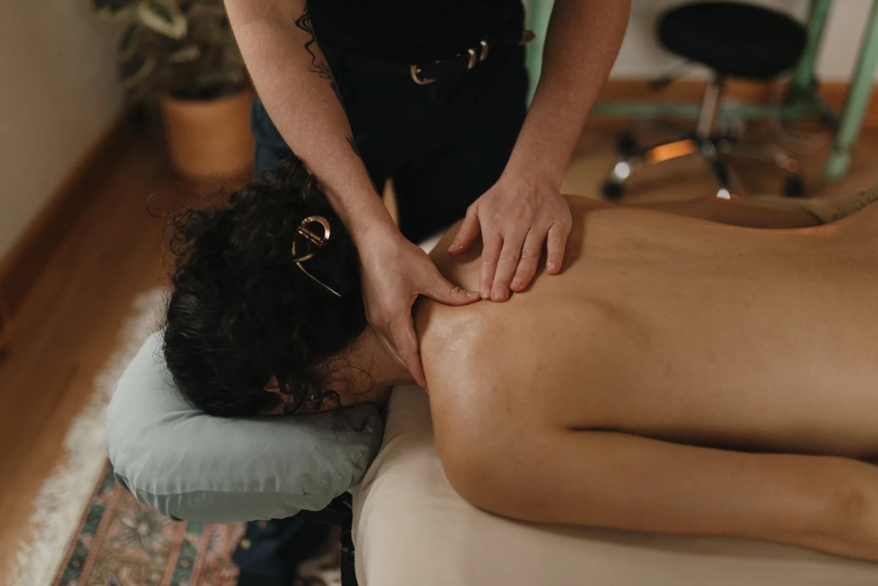 A massage therapist works the neck and shoulder of a patient resting face down in the face cradle.
